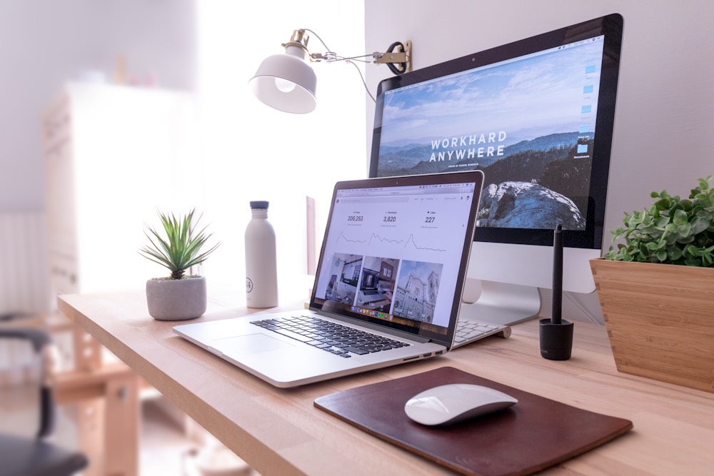 A bright home office with a laptop, desktop computer and plants on a wooden desk